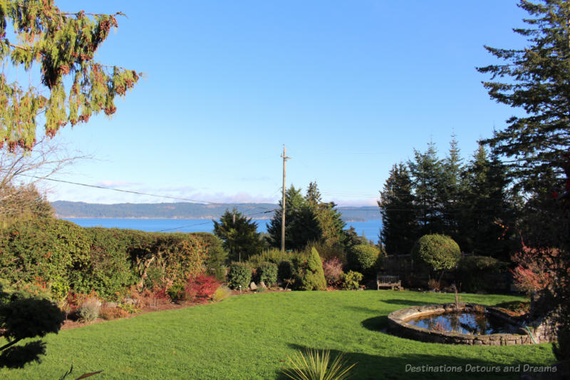 View of landscaped yard l on Salt Spring Island looking out over water with mountains beyond 