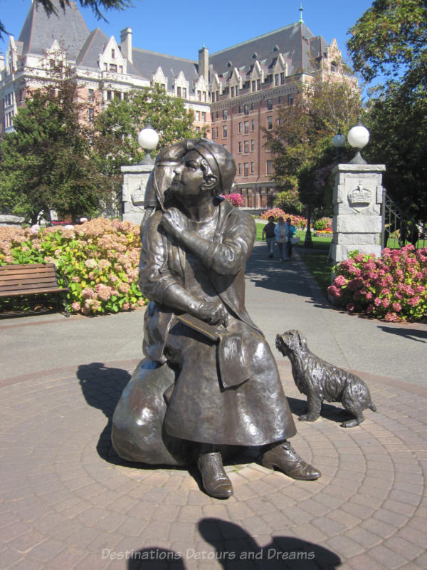 Bronze statue of seated Emily Carr with sketchpad, parrot on shoulder, and dog beside her