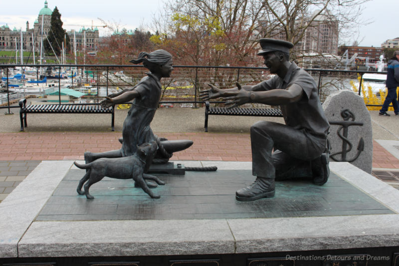 Bronze statue of a little girl and her dog running toward the open arms of her kneeling father in a sailor's uniform