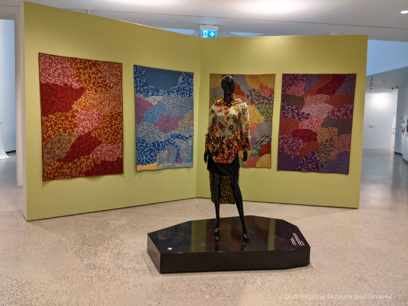 Colourful embroidered Inuit wall hangings depicting the four seasons and a mannequin wearing an embroidered top with beads and pearls at an art exhibition at Qaumajuq