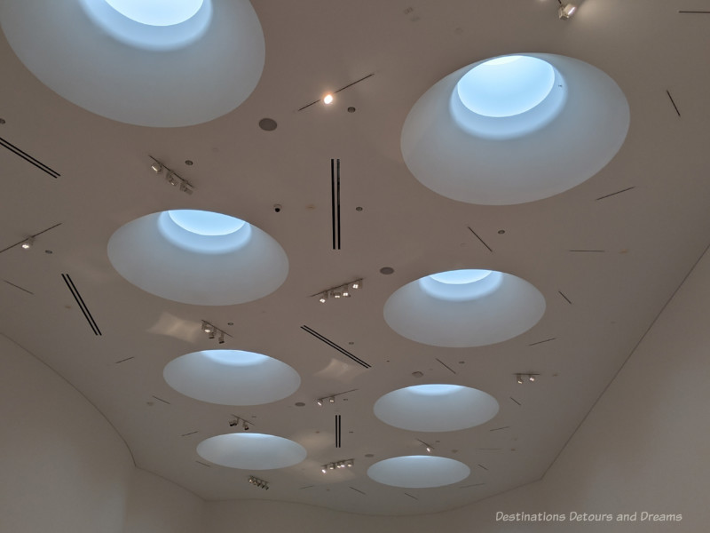 A series of circular skylights in a white ceiling illuminates Qaumajuq Inuit Art Centre