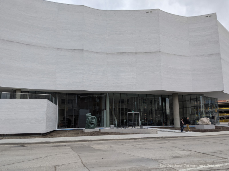 Exterior of Qaumajuq Inuit art centre featuring scalloped white granite and first floor glass paneled walls