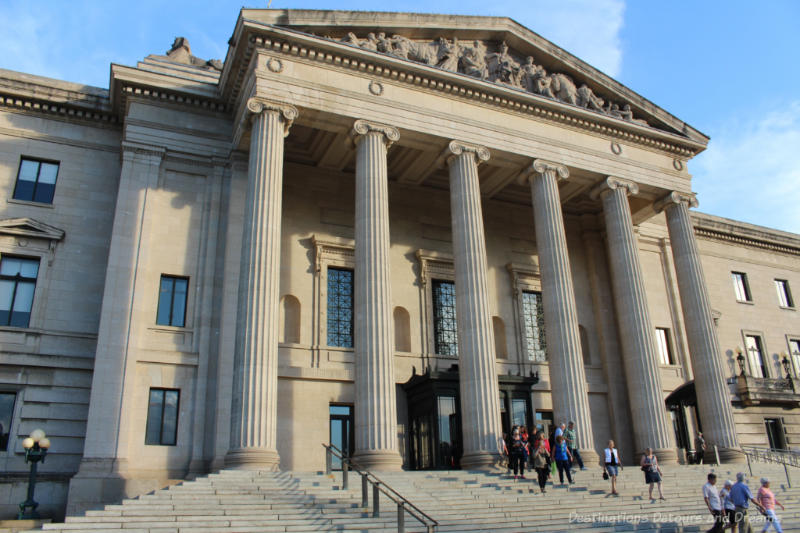 Front of the Beaux-Arts-Classical Manitoba Legislative Building with stone steps, six columns in front of the entrance, and allegorical carvings in the pediment