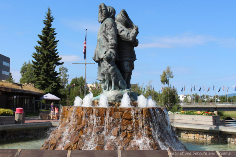 Sculpture of northern family clad in parkas; sculpture is surrounded by a brick encased fountain