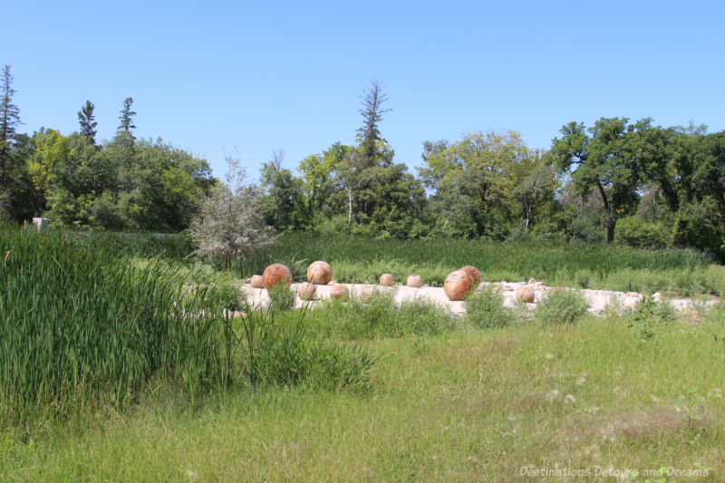 Carved wooden balls sit around a gravel circle amid a landscape of native grasses and shrubs