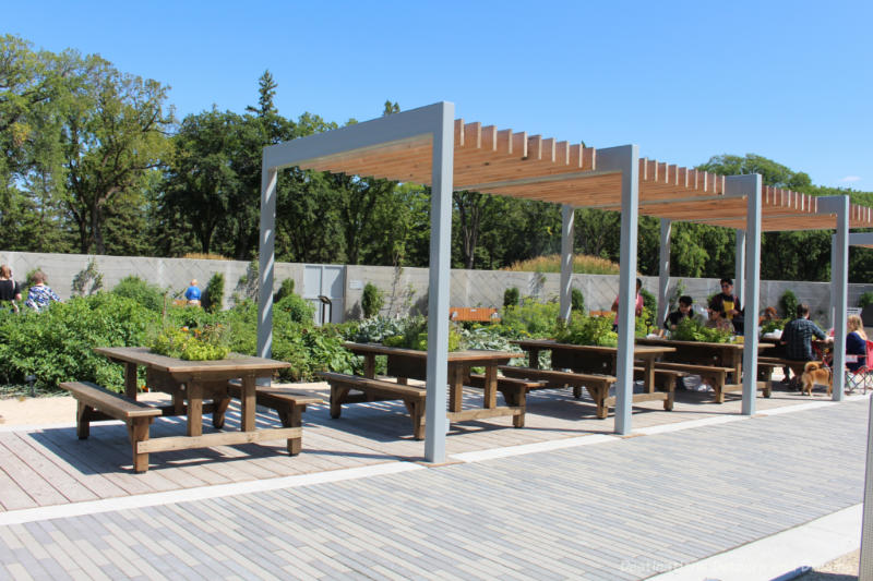 Several picnic tables under a pergola at the Kitchen Garden at Gardens At The Leaf in Winnipeg