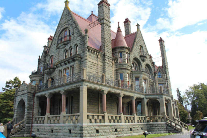 Victoria Craigdarroch Castle Stone castle-like mansion with threee stories, red tiled roof, stained glass windows and wraparound veranda with red stone columns