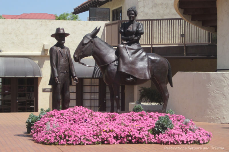 Status of man in cowboy hat standing in front of horse with woman in long skirt side saddle atop horse