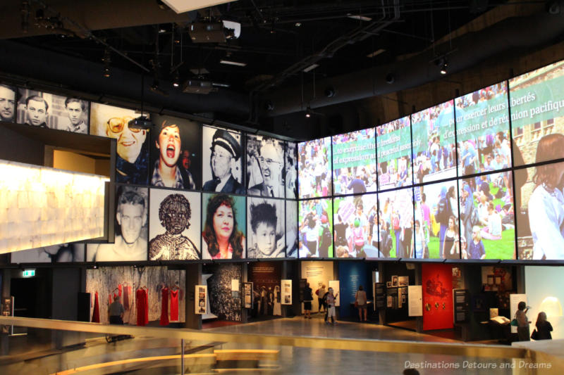 Images of Canadian human rights activists and activities projected on the larger upper wall above displays in CMHR Canadian Journeys gallery