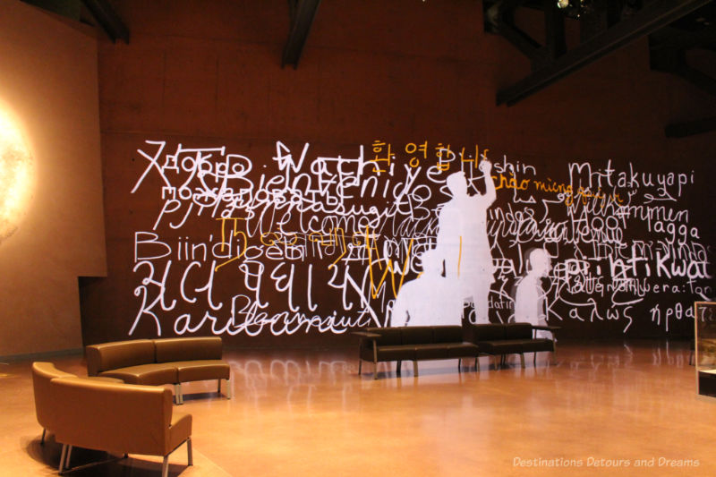 Images of people (shapes only) writing Welcome in many languages along one wall in the entrance hall of the CMHR
