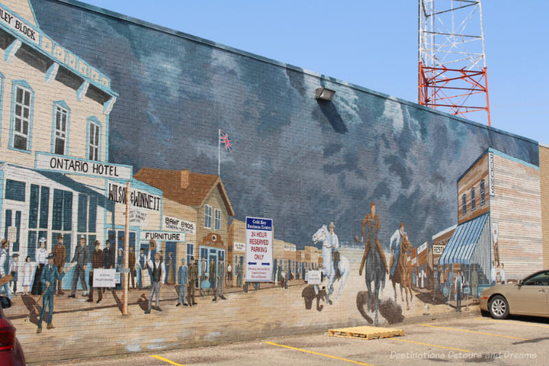 Mural showing a street scene from the 1880s as a prairie storm is on the way with darkening sky, dirt street, wooden buildings lining the street, and men in horses racing down the street