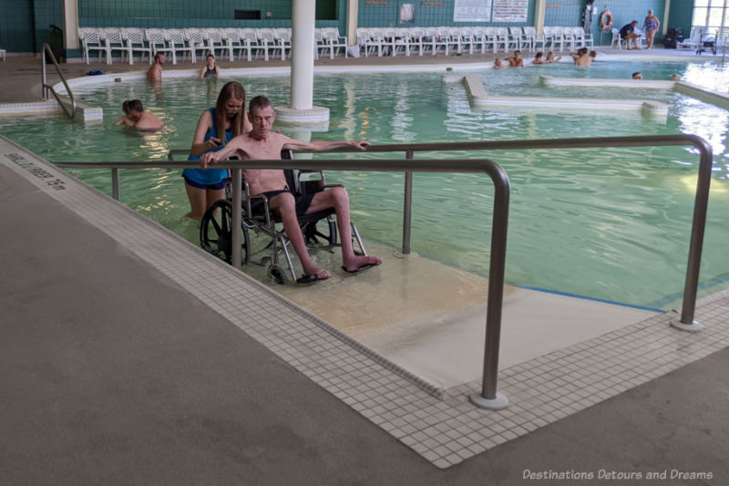 Lifeguard pulling a man in a wheel chair down a ramp into the mineral pool at Temple Gardens Hotel & Spa