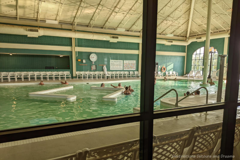 Looking through a window into a large enclosed hotel mineral pool